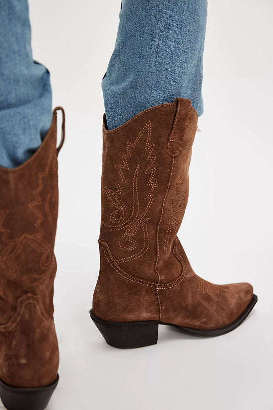 Brown cowboy boots with intricate designs worn with blue jeans on a white background