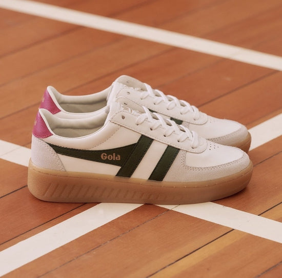 White and green retro-style sneakers by Gola, The shoes feature a white upper with green stripes and a pink heel tab, contrasted against a gum sole.