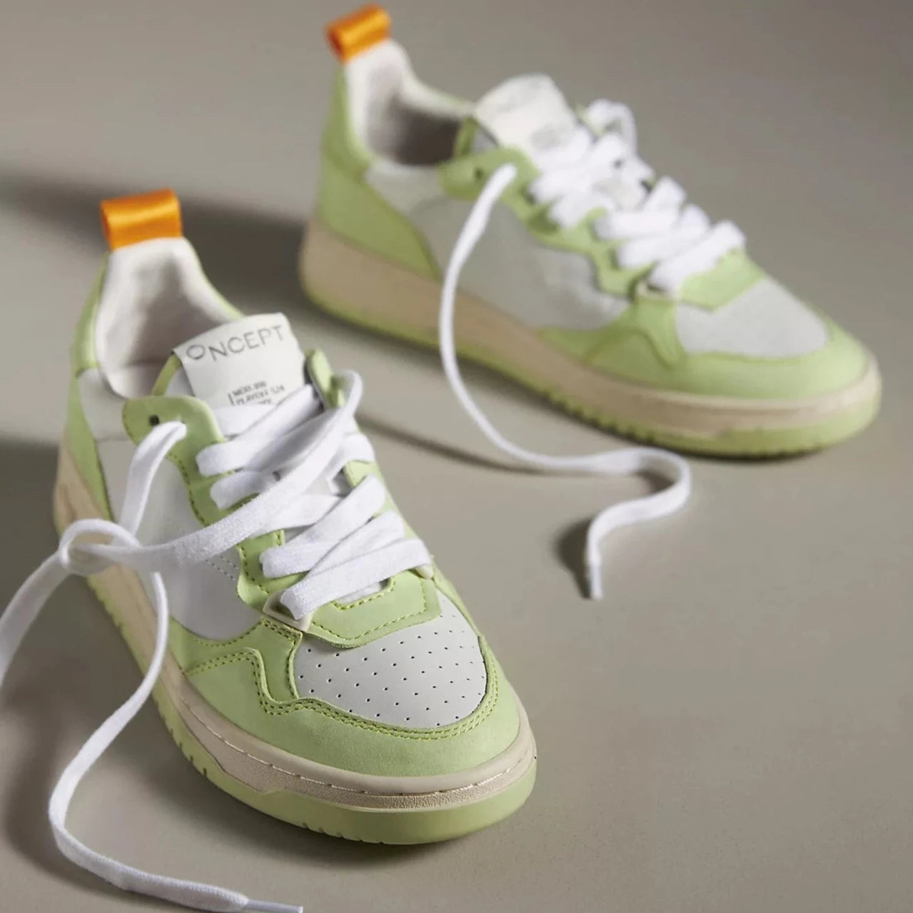 A pair of Oncept Sneakers Phoenix NYC in Green Matcha colorway. The sneakers feature a stylish combination of white and light green leather panels, with white laces and an orange pull tab at the back. 