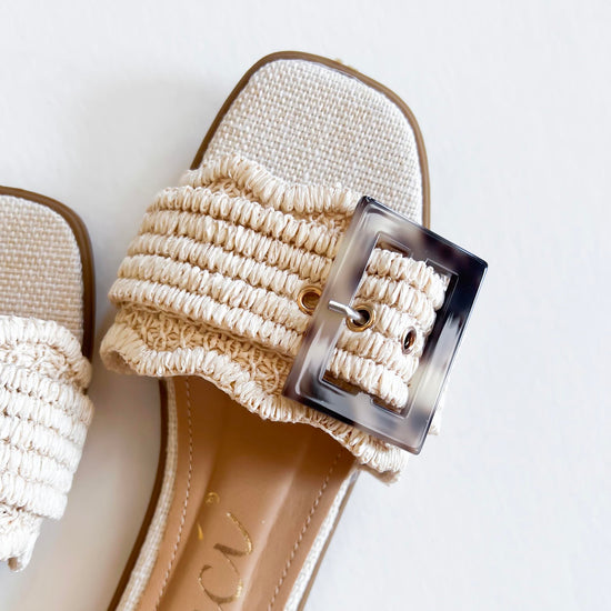 Stylish beige sandals with a textured strap and oversized buckle, perfect for summer fashion