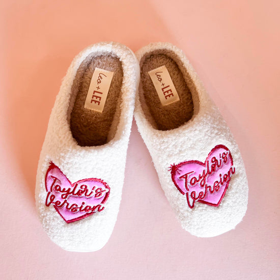 White fleece slippers with pink and red embroidered heart design featuring the words Taylor's Version.
