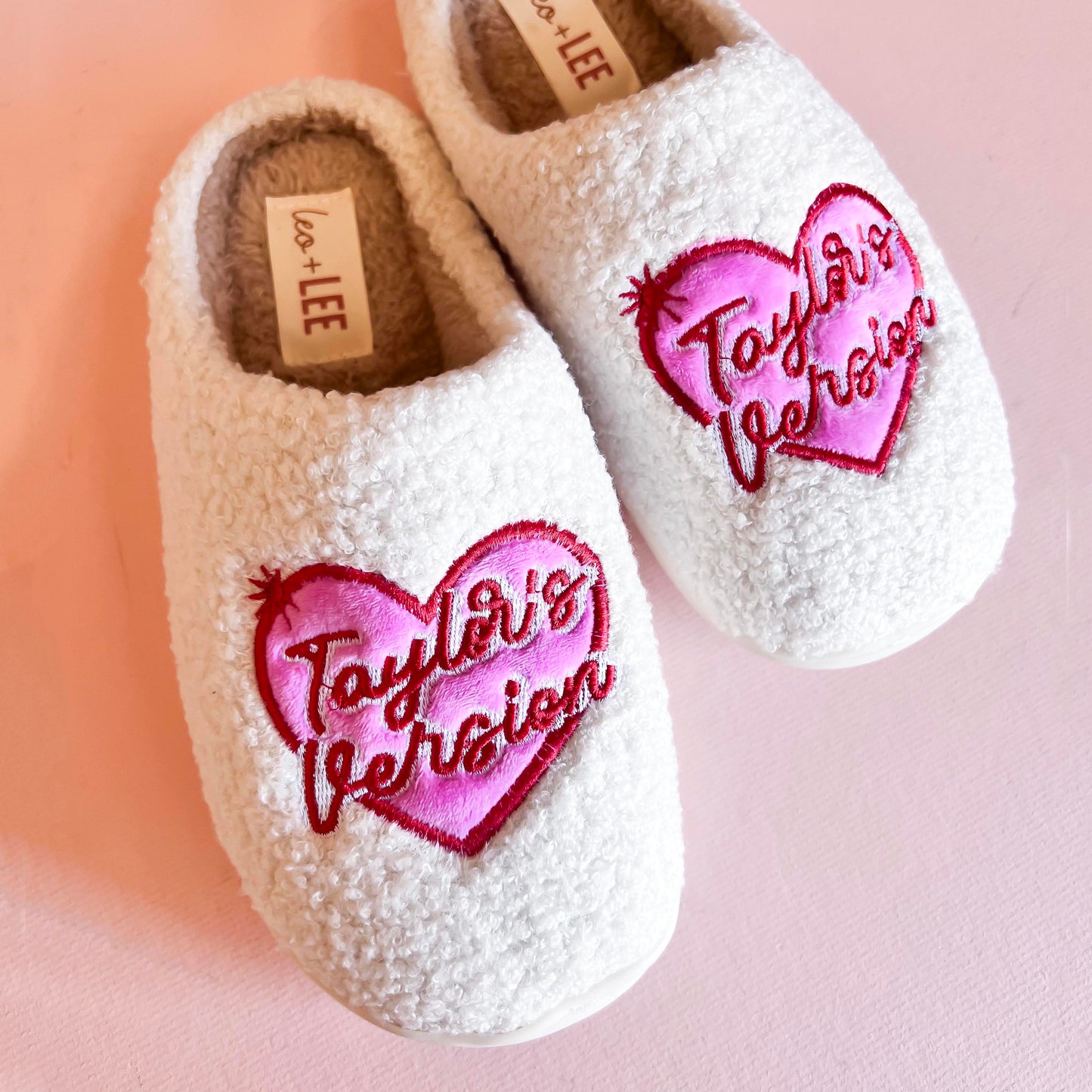 White fleece slippers with pink and red embroidered heart design featuring the words Taylor's Version.