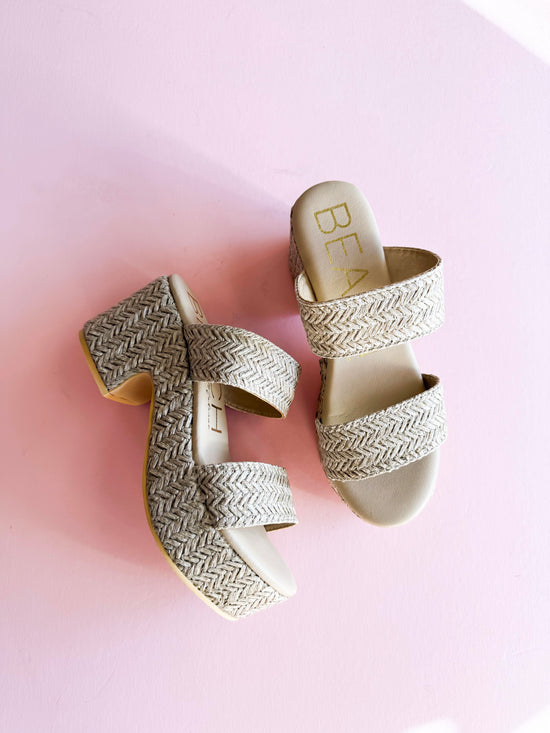 A pair of Beach by Matisse Ocean Ave Platform Sandals with a woven raffia-textured design, featuring double straps and a chunky heel, displayed on a pastel pink background. Stylish and comfortable summer footwear perfect for casual outings and vacations