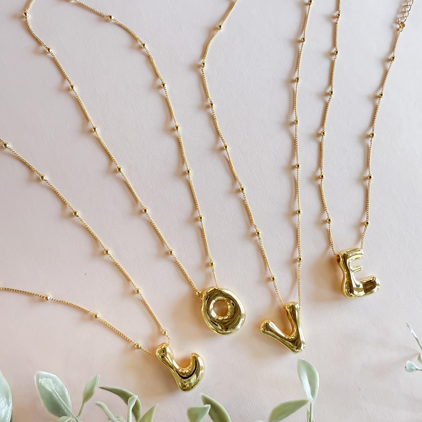 Gold bubble letter necklaces spelling 'LOVE' with a beaded chain, perfect for personalized jewelry and gifting.