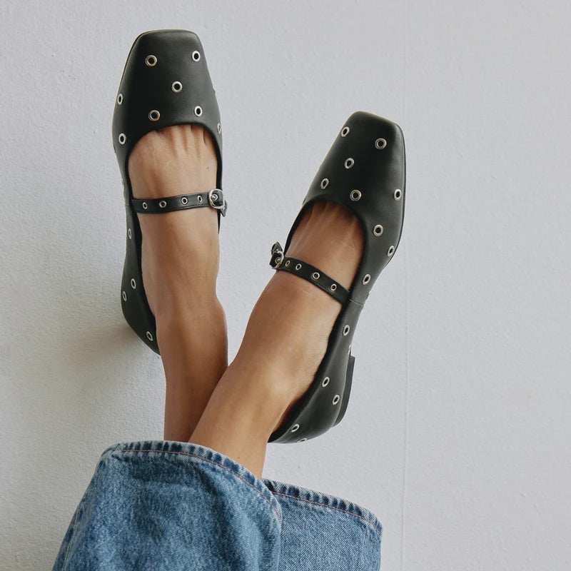 Top view of black studded Mary Jane ballet flats with metal grommets, placed on a model wearing with jeans