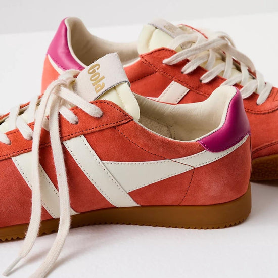 Gola sneakers in a vibrant color scheme of hot coral, off-white, and fuchsia. The shoes have a classic retro design with suede material and a gum rubber sole. The brand name "Gola" is prominently displayed on the side and tongue of the sneakers in gold lettering. The laces and stripes are off-white, providing a striking contrast to the bold coral and fuchsia colors.