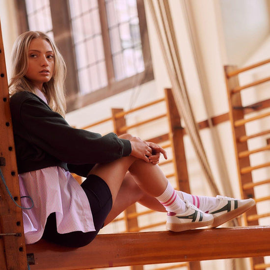 White and green retro-style sneakers by Gola, The shoes feature a white upper with green stripes and a pink heel tab, contrasted against a gum sole.