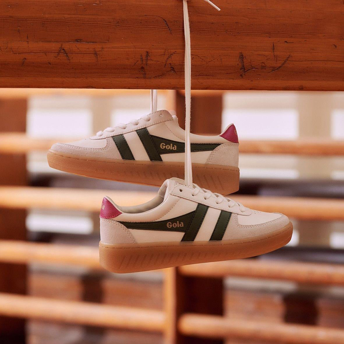 White and green retro-style sneakers by Gola, The shoes feature a white upper with green stripes and a pink heel tab, contrasted against a gum sole.