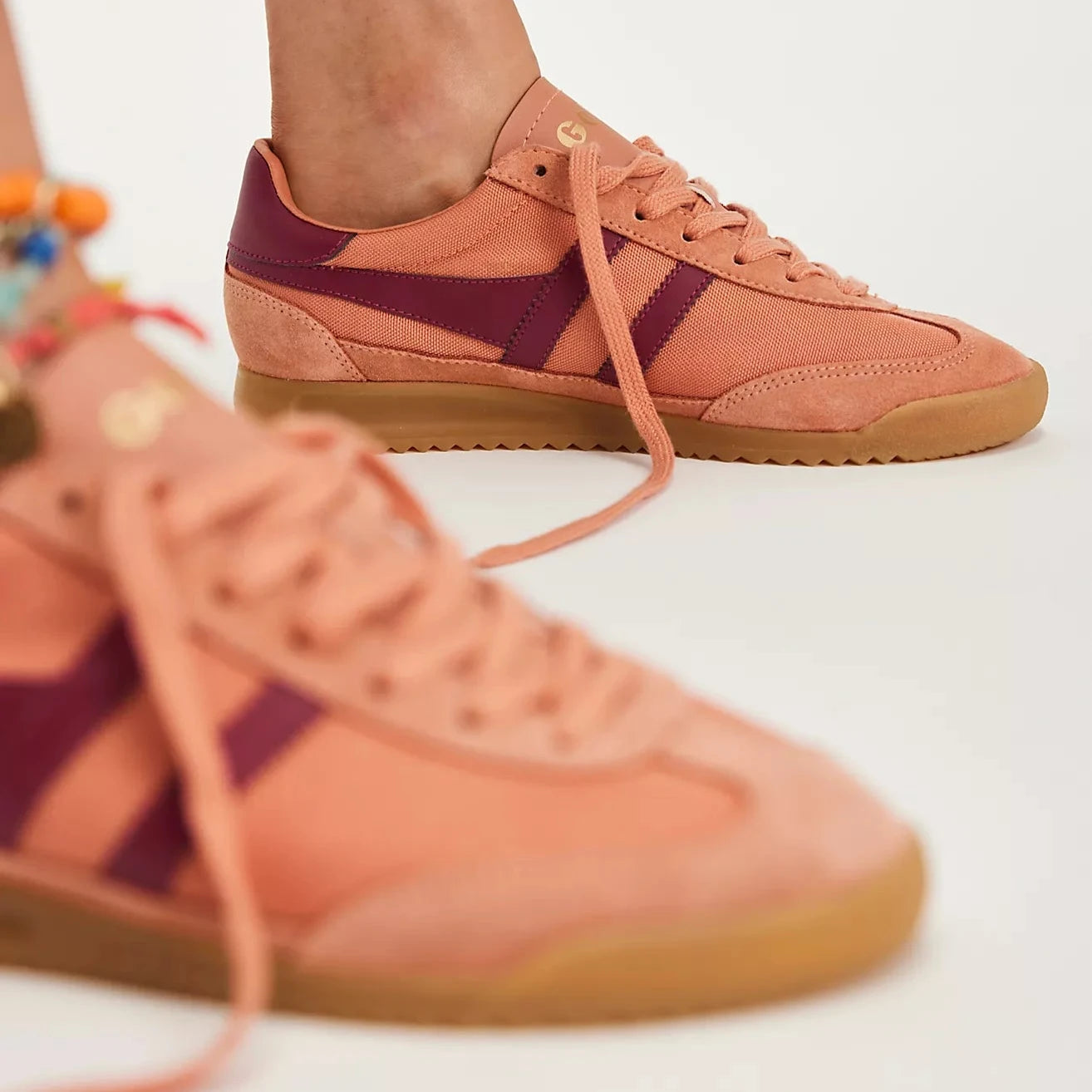 Side view of a Gola Tornado sneaker featuring a terracotta canvas and suede upper, burgundy leather stripes, gold Gola branding, and a gum rubber sole.