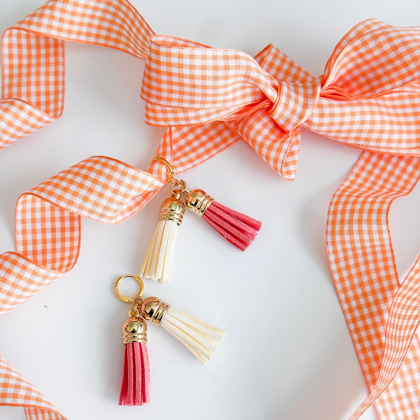 Tassel keychain with pink and gold accents on an orange checkered ribbon background