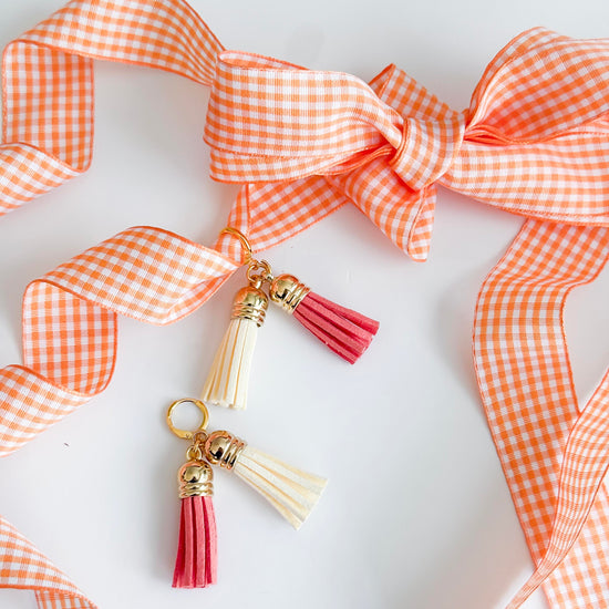 Tassel keychain with pink and gold accents on an orange checkered ribbon background