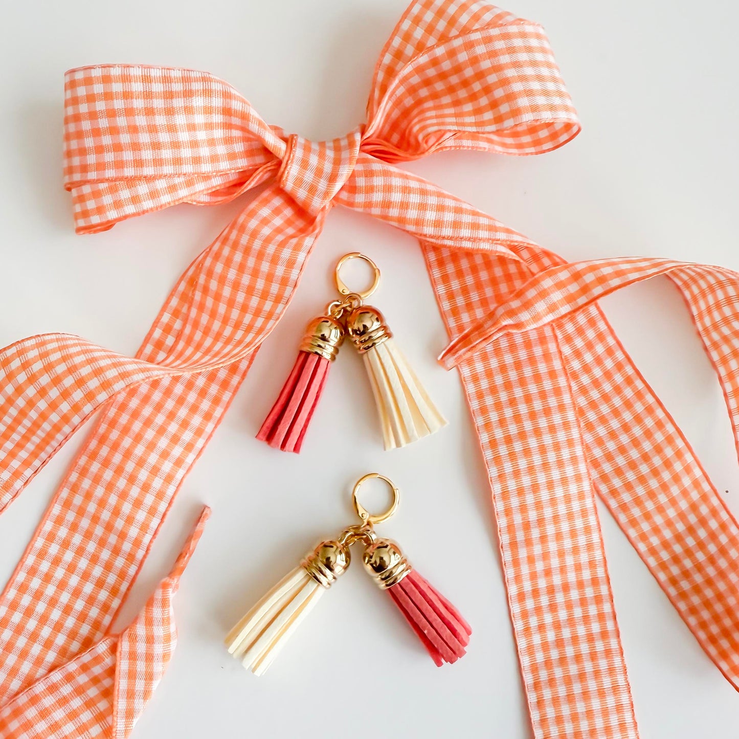 Two tassel charms with gold accents on a white background with an orange checkered ribbon.
