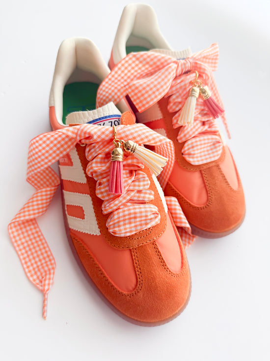 Orange shoes with pink gingham ribbons and tassels on a white background