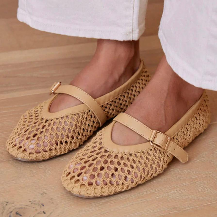 Woven mesh Mary Jane flats with a beige buckle strap, worn with white pants on a wooden floor.