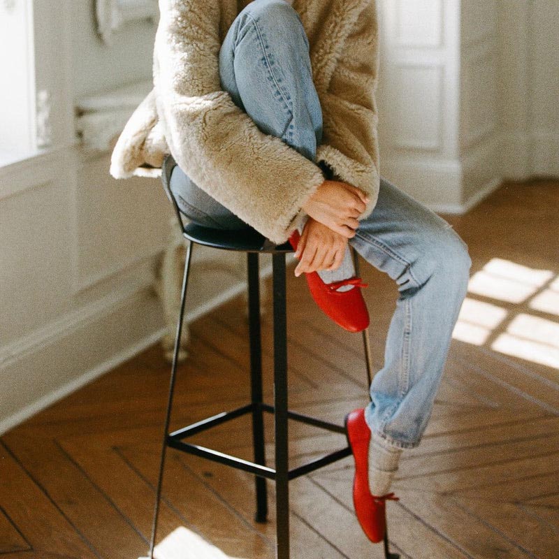 Red leather ballet flats with a square toe design and bow detail showcased on a model. 