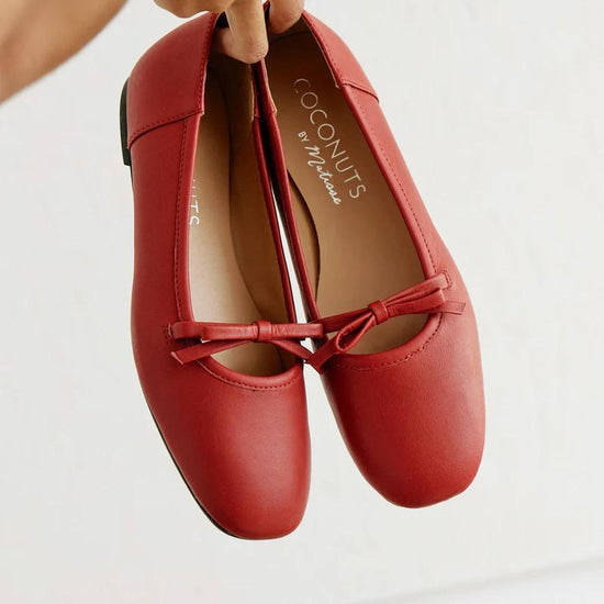 Red leather ballet flats with a square toe design and bow detail, held up against a neutral background