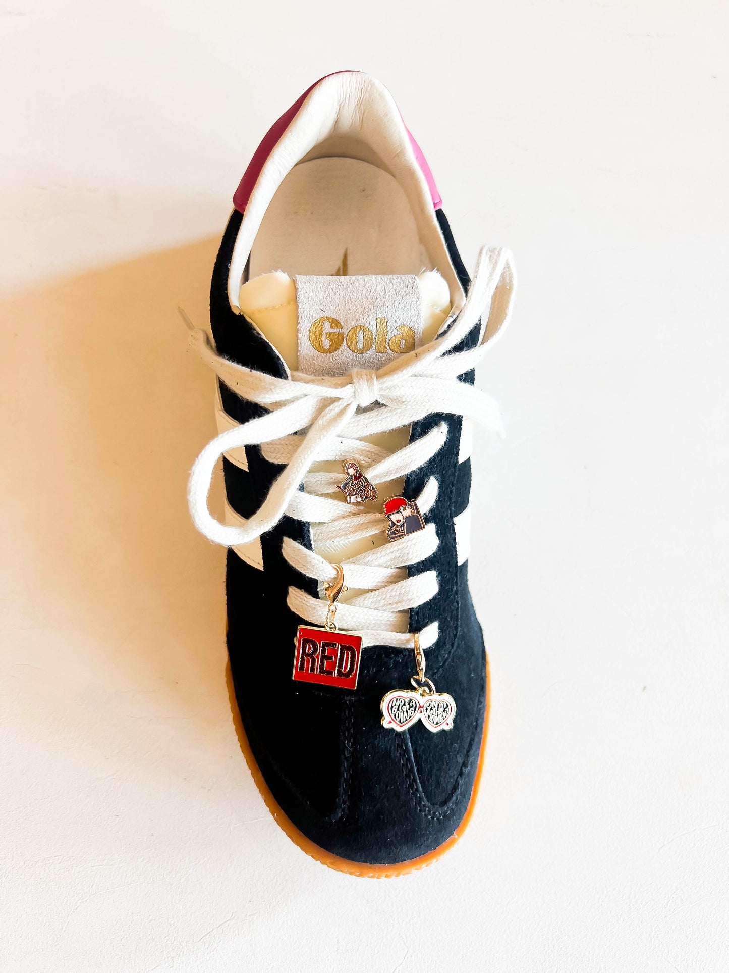 Sneaker with custom Swiftie-themed charms on cream-colored laces, featuring a 'RED' square charm, heart-shaped sunglasses charm, and two additional playful designs displayed next to extra laces.